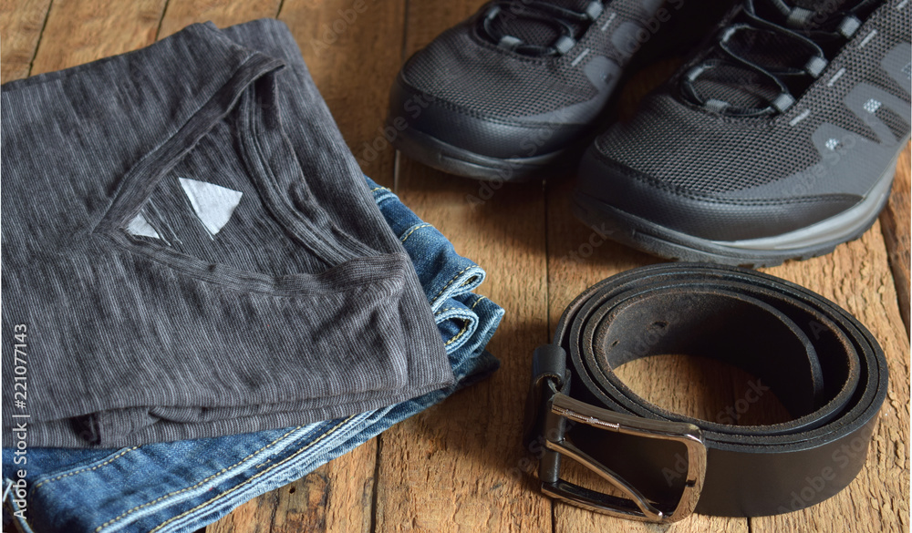 Men's casual outfits. Men shoes, clothing and accessories on wooden background - grey t-shirt, blue jeans, sneakers, belt. Top view. Flat lay. Men's casual outfits. Men shoes, clothing and accessories on wooden background - grey t-shirt, blue jeans, sneakers, belt. Top view. Flat lay.