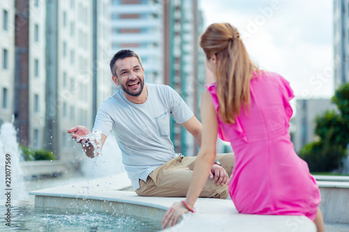 Joyful mood. Happy delighted man playing with the water while looking at his girlfriend