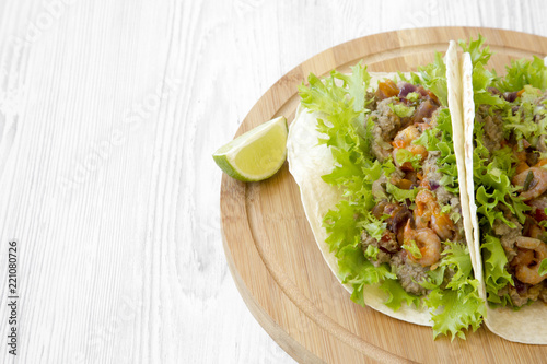Shrimp tacos on round bamboo board on white wooden background, low angle view. Mexican food. Space for text.