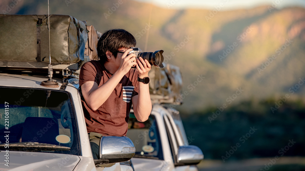 Young Asian male traveler and photographer sitting on the car window taking photo on road trip in Namibia, Africa. Travel photography concept - obrazy, fototapety, plakaty 