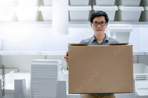 Young Asian man carrying cardboard box choosing what to buy. Warehouse shopping concept