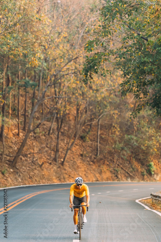 full face photo of Asian man in yellow cycling jersey, who riding on road bike up high on hill. Cycling in the morning, under morning sunlight with fresh air.