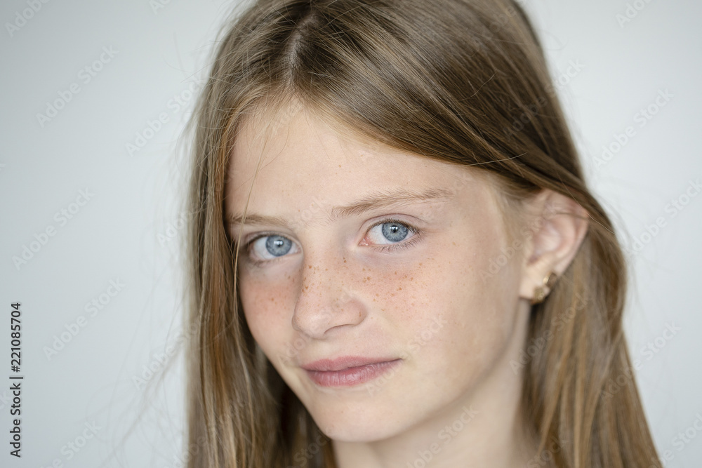 Beautiful blond young girl with freckles indoors on white wall background, closeup portrait Beautiful blond young girl with freckles indoors on white wall background, closeup portrait