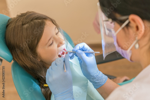 Cute little girl lying in a dentist chair and smiling at the camera while having an oral cavity checkup conducted by a dentist using a probe. Little girl sitting in the dentists office