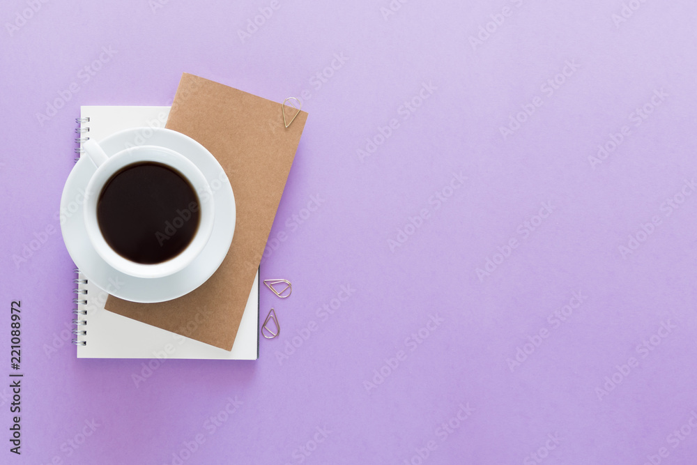 Top view over the working desk with notebook, cup of coffee. Copy space for text. Flat lay of a workplace on light violet background Top view over the working desk with notebook, cup of coffee. Copy space for text. Flat lay of a workplace on light violet background