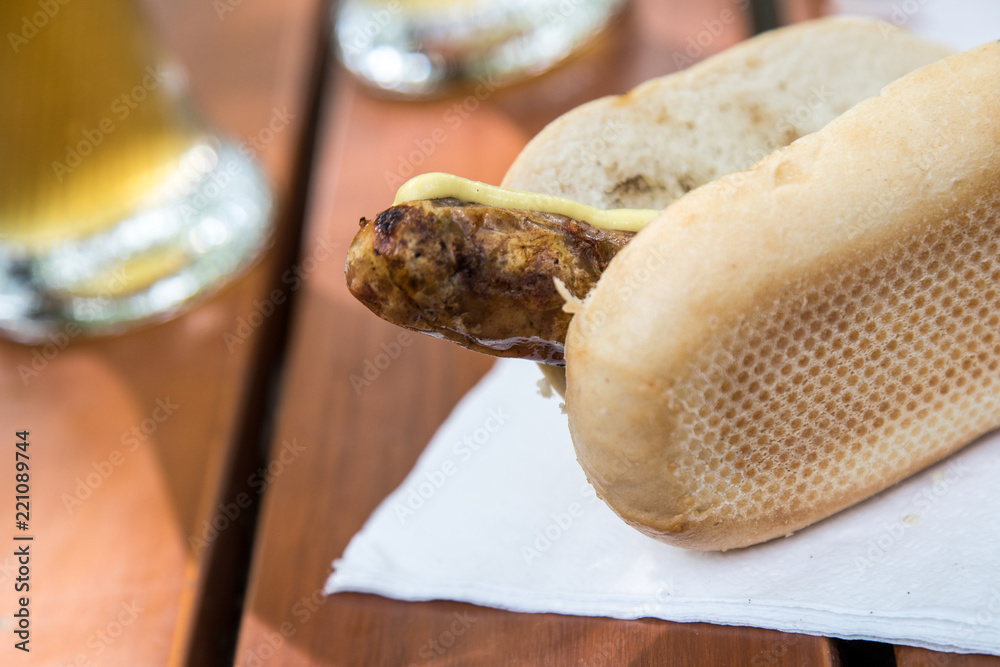 Schweinefleisch Bratwurst vom Grill mit Senf im Weizen Brötchen und Bier im Biergarten Schweinefleisch Bratwurst vom Grill mit Senf im Weizen Brötchen und Bier im Biergarten