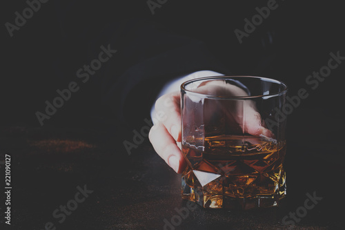 Whiskey glass in hand on the dark bar counter, selective focus