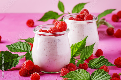 Raspberry smoothie in glass jar with fresh berry and greek yogurt on pink stone background, selective focus