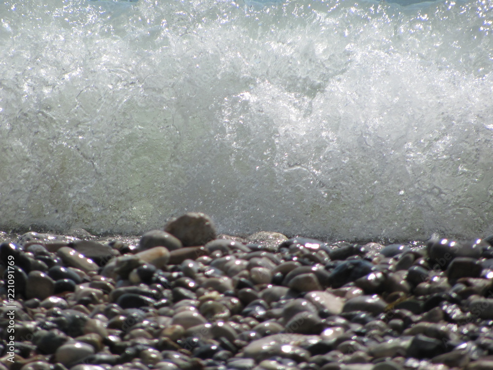 Fototapeta premium The shore of the sea close-up: a pebble from a pebble with sand and an incident wave. Beautiful background.