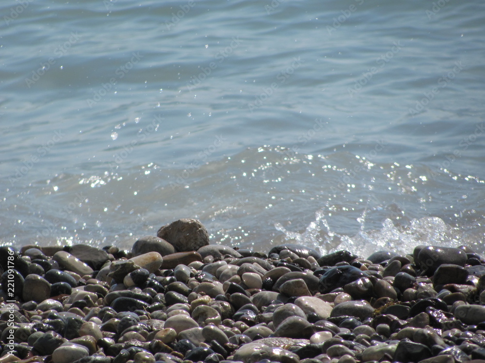 The shore of the sea close-up: a pebble from a pebble with sand and an incident wave. Beautiful background. The shore of the sea close-up: a pebble from a pebble with sand and an incident wave. Beautiful background.