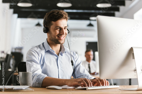 Fotomurale Photo of businesslike man 20s wearing office clothes and headset, working on com