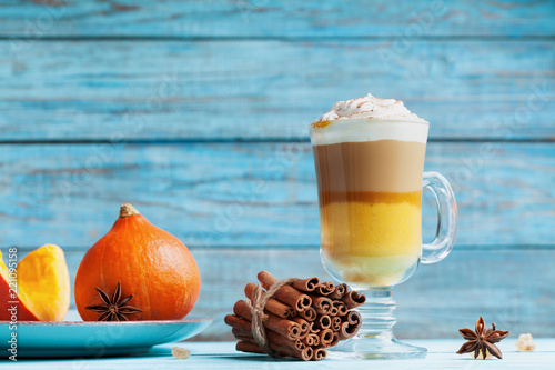 Pumpkin spiced latte or coffee in glass on turquoise rustic table. Autumn, fall or winter hot drink.