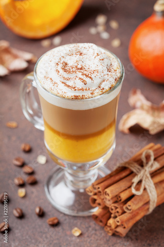 Pumpkin spiced latte or coffee in glass on brown background. Autumn, fall or winter hot drink.