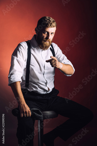 Portrait on a bearded man in white shirt and suspenders on black background in studio