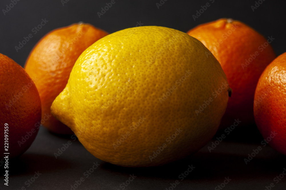 Yellow ripe lemon with four mandarin oranges in the background over black. Shallow dof. Yellow ripe lemon with four mandarin oranges in the background over black. Shallow dof.