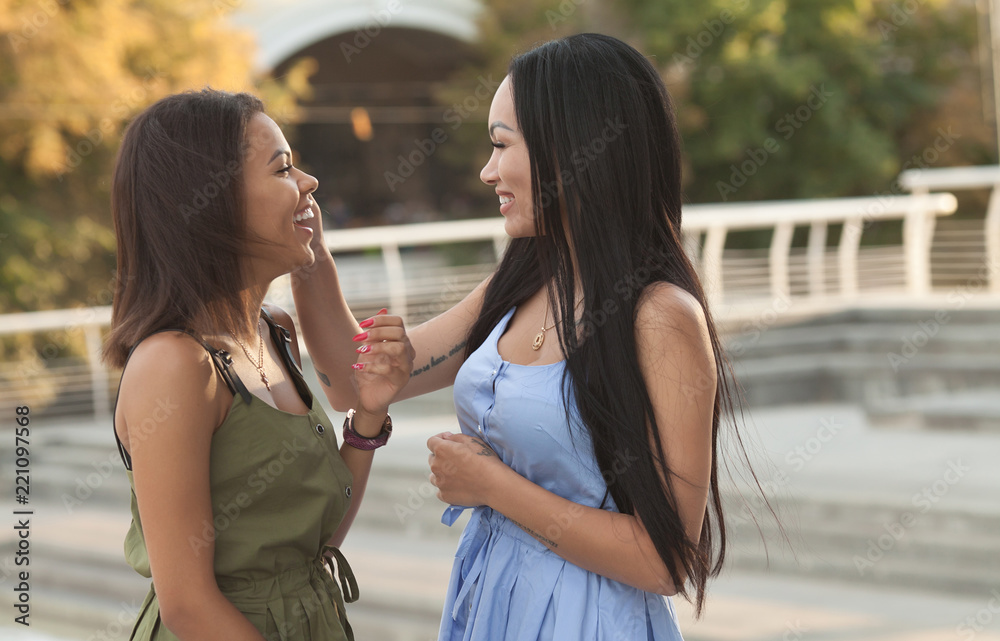 Outdoors portrait of two female multiethnic friends. Girls in casual outfits having a walk in the city, having fun and hugging, copy space. Urban lifestyle, friendship concept
