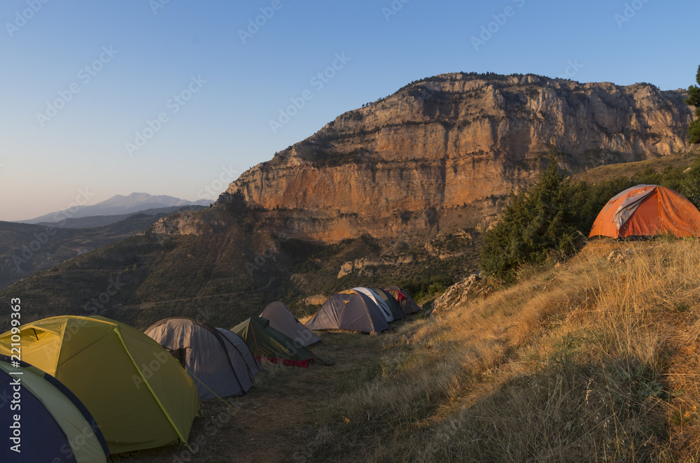 The camping in the mountains at sunrise under the morning clear blue sky; Group of tourist tents against the background of the mountains at dawn