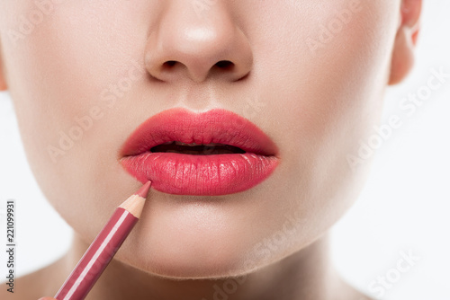 partial view of woman applying pink lip pencil, isolated on white