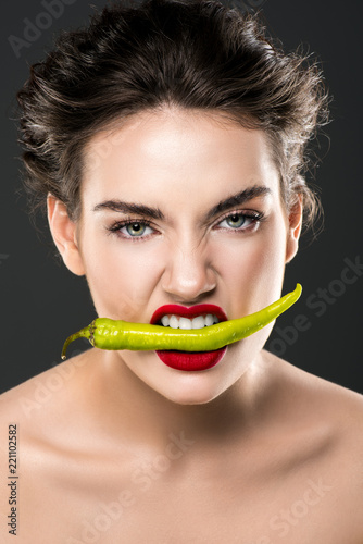 portrait of woman holding green chili pepper in teeth, isolated on grey