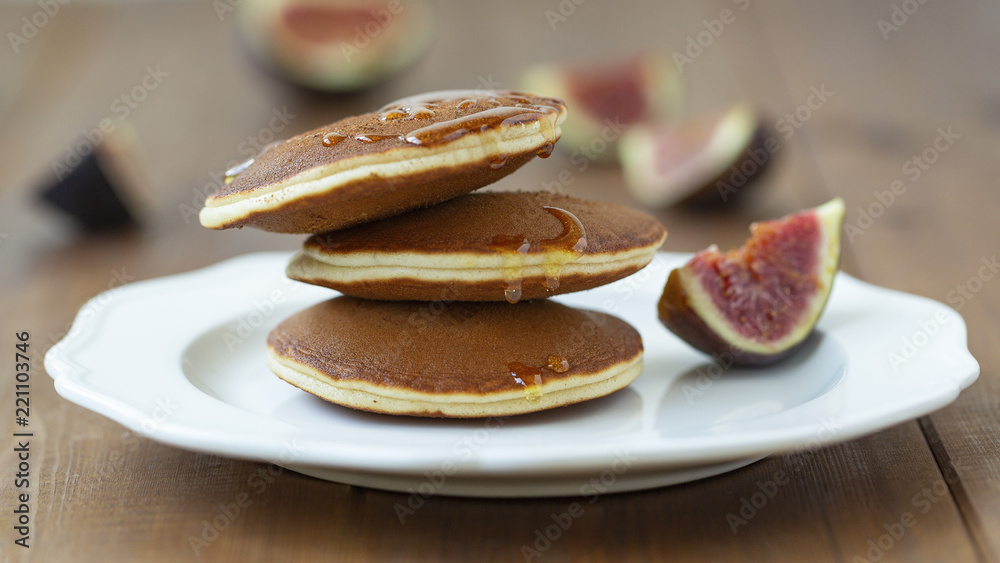 Pancakes with figs and honey on a white plate. On a wooden table