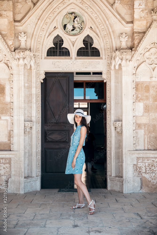 Brunette girl in blue summer dress walking on old narrow street