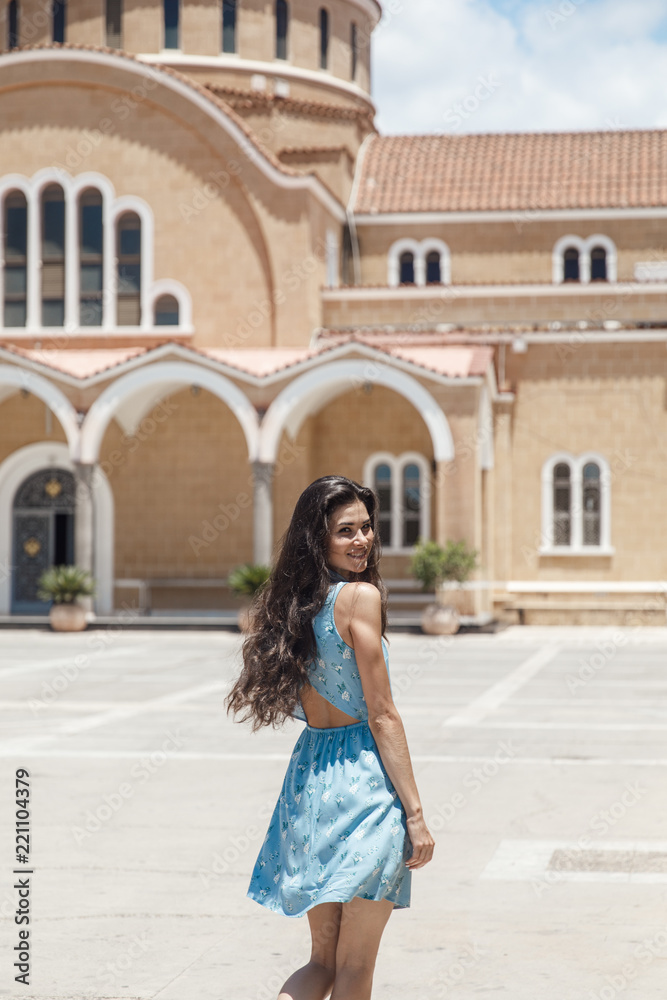 Brunette girl in blue summer dress walking on old narrow street