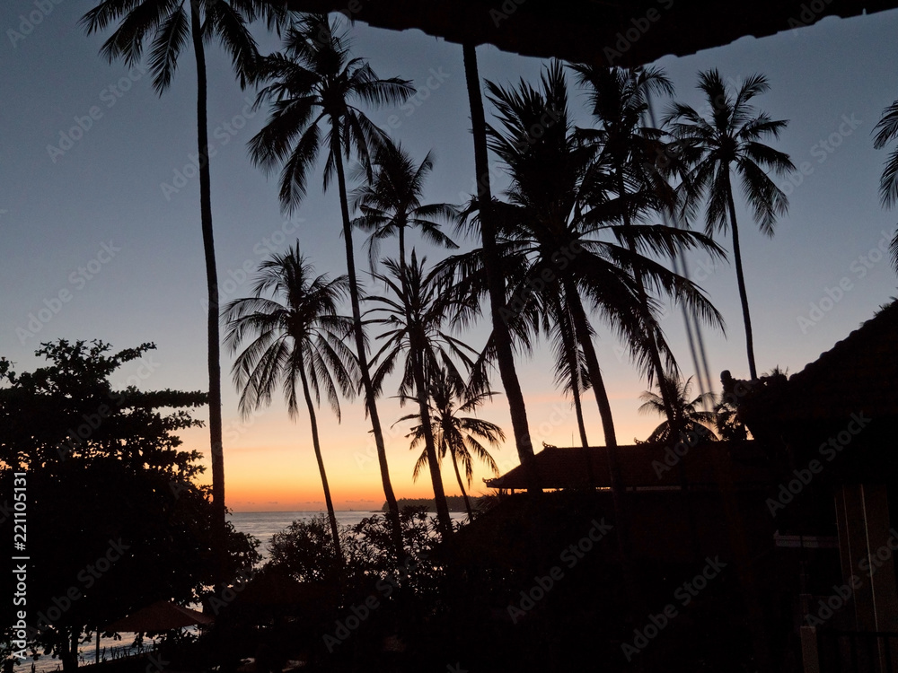 Sunset, silhouette of palm trees. Travel concept, palm trees on the background of the sea at sunset time. Sunset on the ocean coast, mountains, sea, beach, sky, clouds Bali, Indonesia.