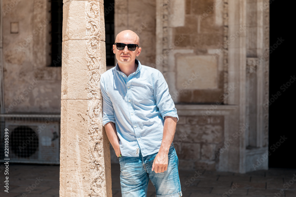 Obraz premium Bald man in sunglasses walking on old narrow street