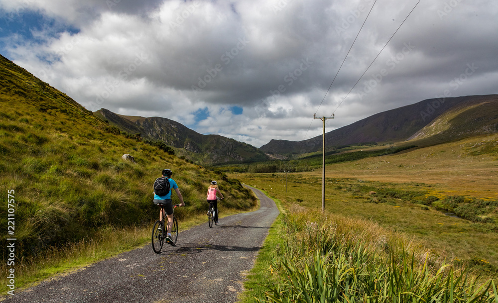 Active couple biking on a rural country road  in the scenic mountain valley landscape of the Dingle peninsula, County Kerry in the Republic of Ireland