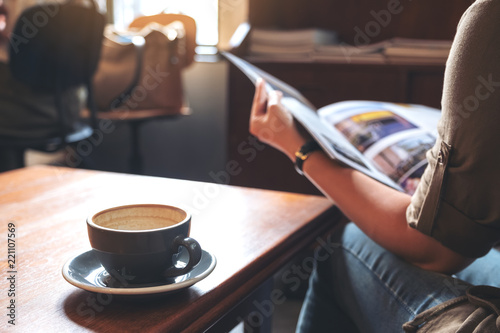 Closeup image of a woman reading a book with coffee cup on wooden table in modern cafe