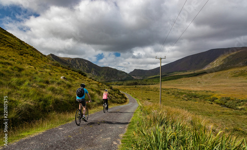 Active couple biking on a rural country road in the scenic mountain valley landscape of the Dingle peninsula, County Kerry in the Republic of Ireland