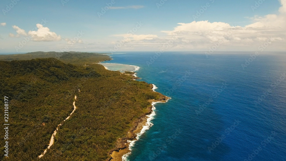 Aerial view: sea and the tropical island with rocks, beach and waves. Coastline of the tropical island Siargao with the mountains and the rainforest on a background of ocean with big waves. Seascape