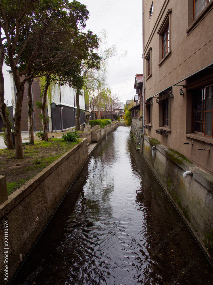 Wide detail of concrete buildings and trees along the canals near Kurokabe Square. Nagahama, Shiga, Japan. Vertical orientation. Travel and architecture.