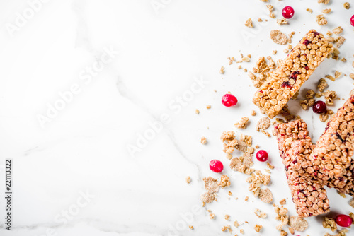 Multi grain granola muesli bar. Healthy sweet food, diet snack, with dried berries, nuts, cereals and honey. On a white marble background, top view copy place for text.