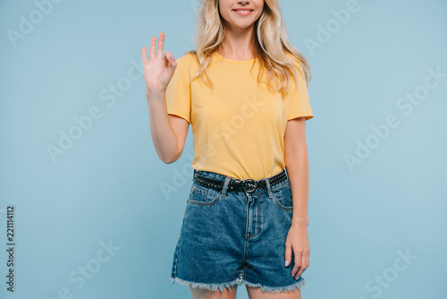 cropped image of girl in shirt and shorts showing okay gesture isolated on blue