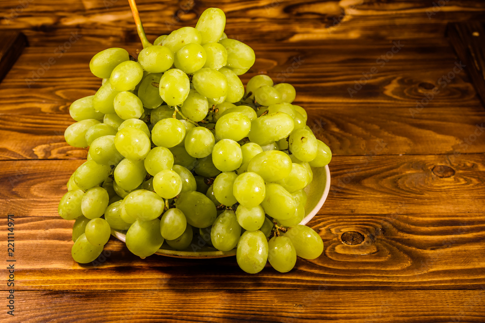 Ceramic plate with green grapes on wooden table Ceramic plate with green grapes on wooden table