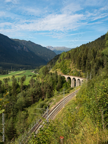 Train and the bridge in Switzerland with green slopes. The Rhaetian Railway section from the Albula/Bernina area (the part from Thusis to Tirano, including St Moritz), August, 2018