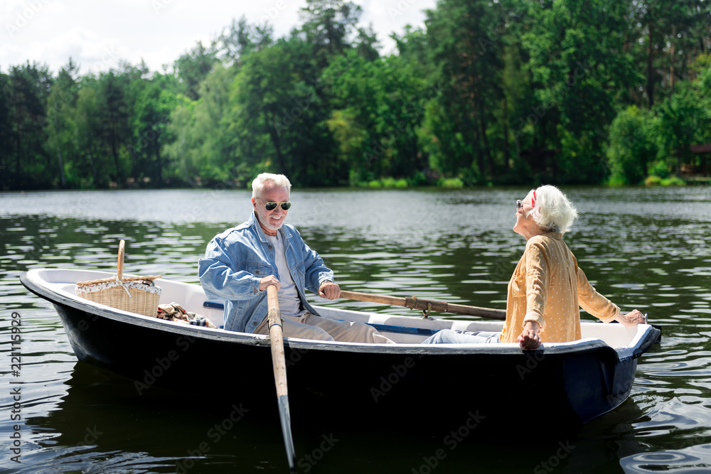 Paddles and boat. Happy elderly man holding paddles while sitting in boat with his appealing stylish wife Paddles and boat. Happy elderly man holding paddles while sitting in boat with his appealing stylish wife