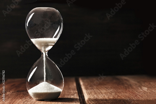 A side view of an hourglass with falling sand, on a dark background with copy space