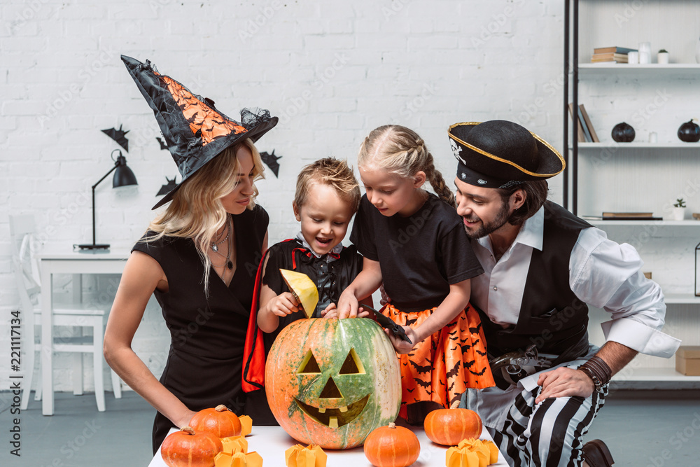 Fototapeta premium family in various halloween costumes at table with pumpkins in kitchen at home