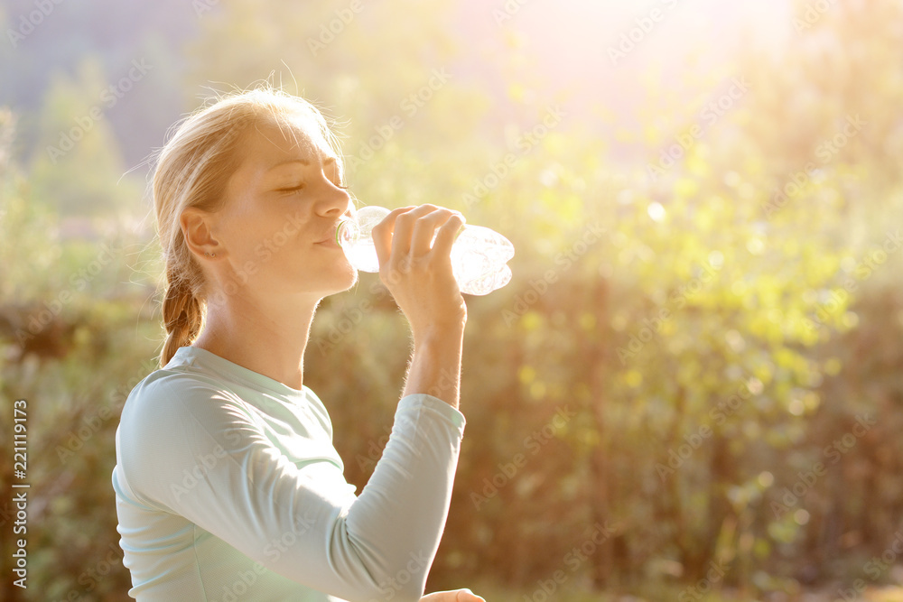 Young sporty woman after workout and running drinks water on a sunny day