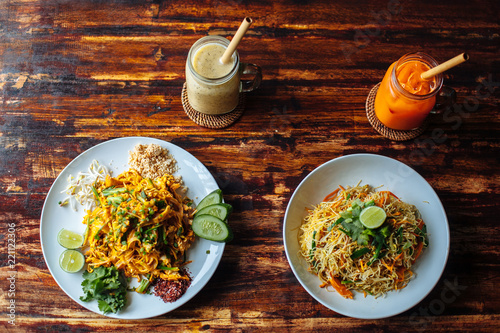 Healthy Vegetarian vegan menu Pad Thai, stir-fried rice noodles and singapore noodles and banana and carrot smoothies on wooden table.top view photo