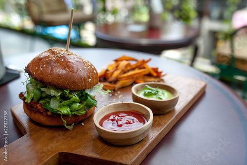 Fast food. Vegetarian burger with a chop, lettuce with sweet potatoes fries and two sauces. Tasty sandwich for lunch on wooden table in cafe. concept of health food