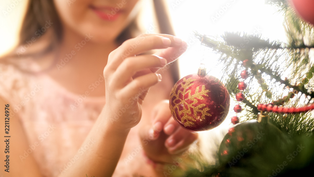 Naklejka premium Closeup photo of smiling teenage girl hanging glass balls on Christmas tree