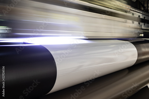 Massive print head flashing by while processing a big oversized roll of glossy premium paper in a professional plot and print facility.