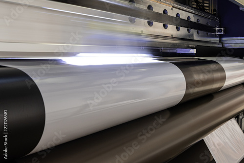 Massive print head flashing by while processing a big oversized roll of glossy premium paper in a professional plot and print facility.