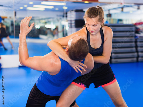 Woman is training captures with man on the self-defense course in gym.