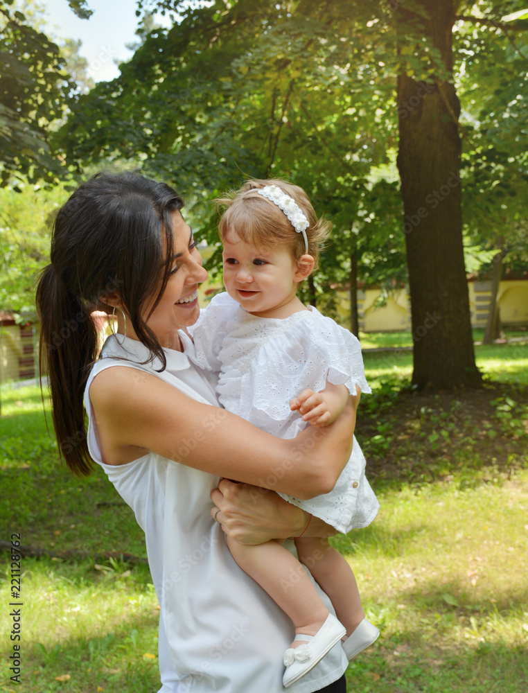 Happy Woman Hugging her Baby Girl with White Dress in the Summer Park . Happy Woman Hugging her Baby Girl with White Dress in the Summer Park .