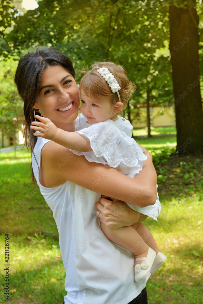 Happy Woman Hugging her  Baby Girl with White Dress in the Summer Park .