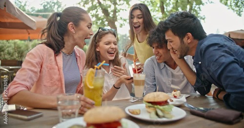 Five multiethnic friends sitting at table in cafe, talking on phone with someone, and laughing. People enjoying theit time together 4k photo